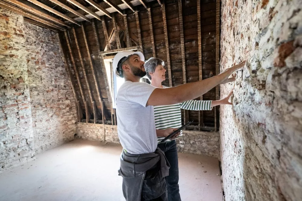 Architecte et artisan examinant un mur ancien en brique et pierre avant une isolation par l'intérieur